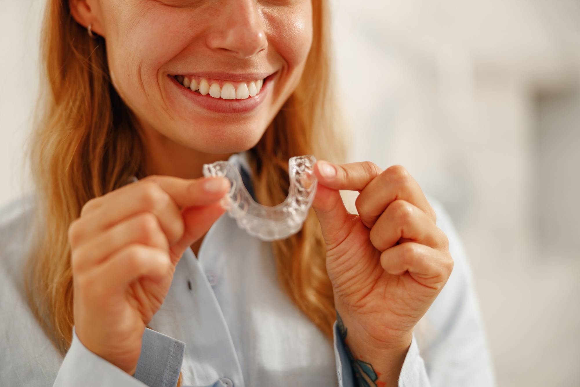 A Smiling Woman Proudly Holding Clear Dental Aligners that Help Achieve a Perfect Smile
