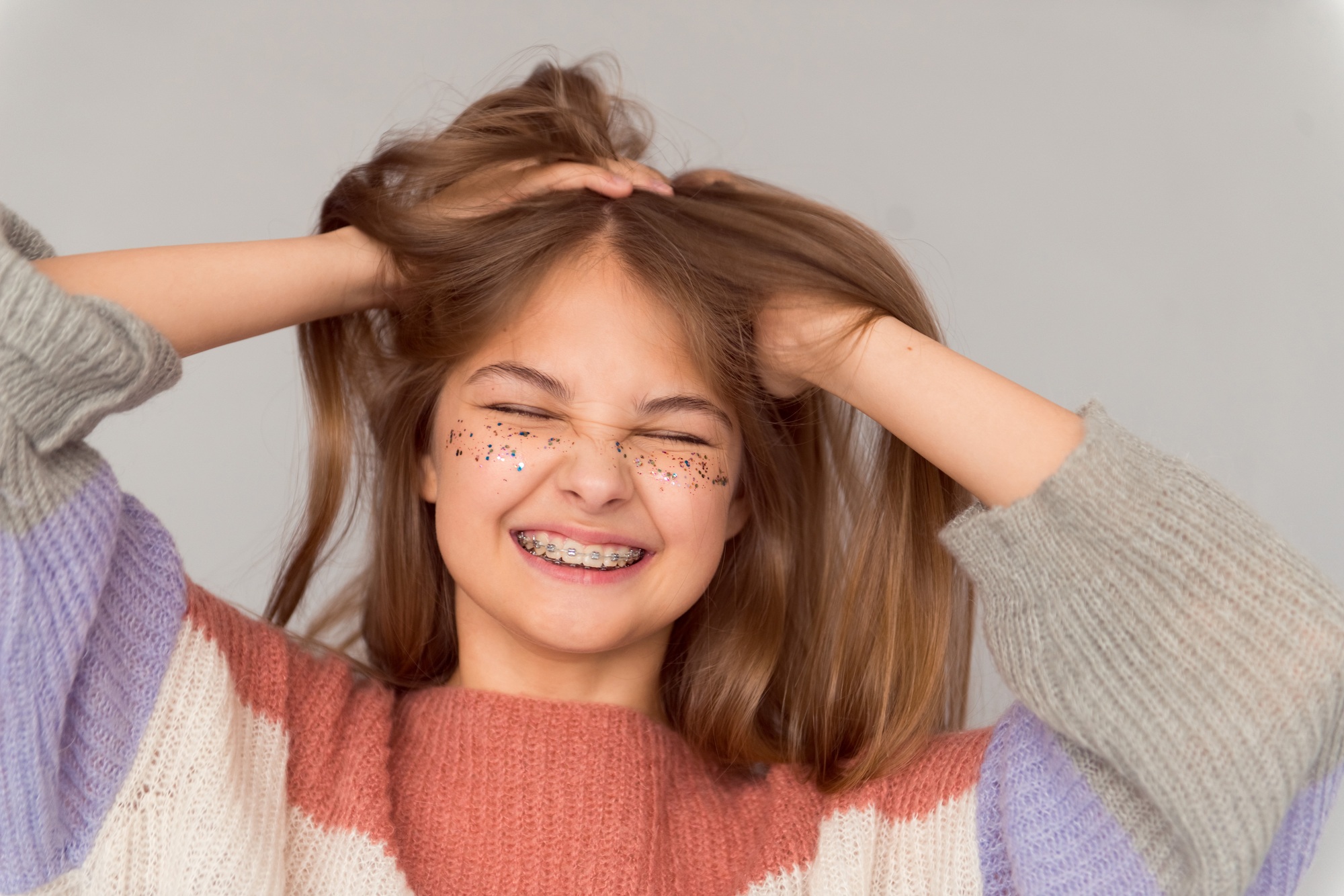 Beautiful happy teen girl with shiny freckles on face and braces holding head and smiling