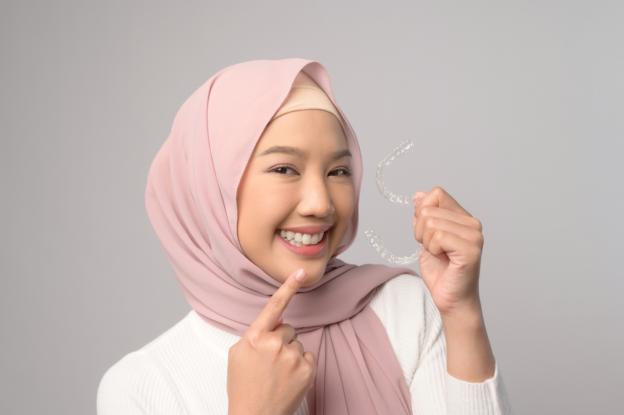 Muslim woman with hijab holding invisalign braces in studio