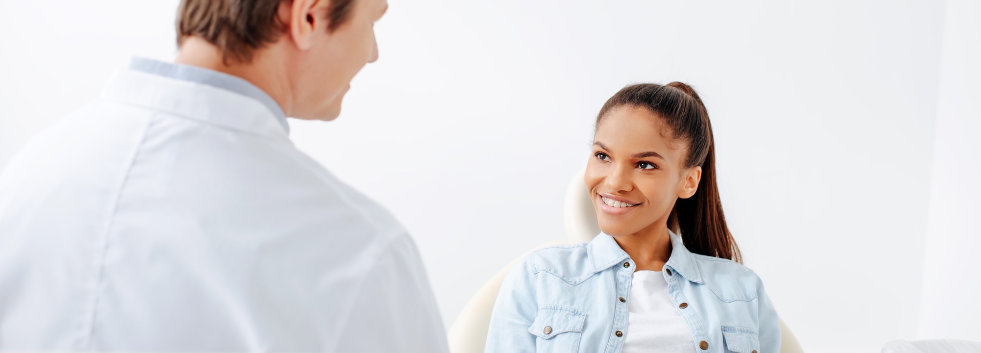 panoramic shot of happy african american woman in braces looking at orthodontist in clinic