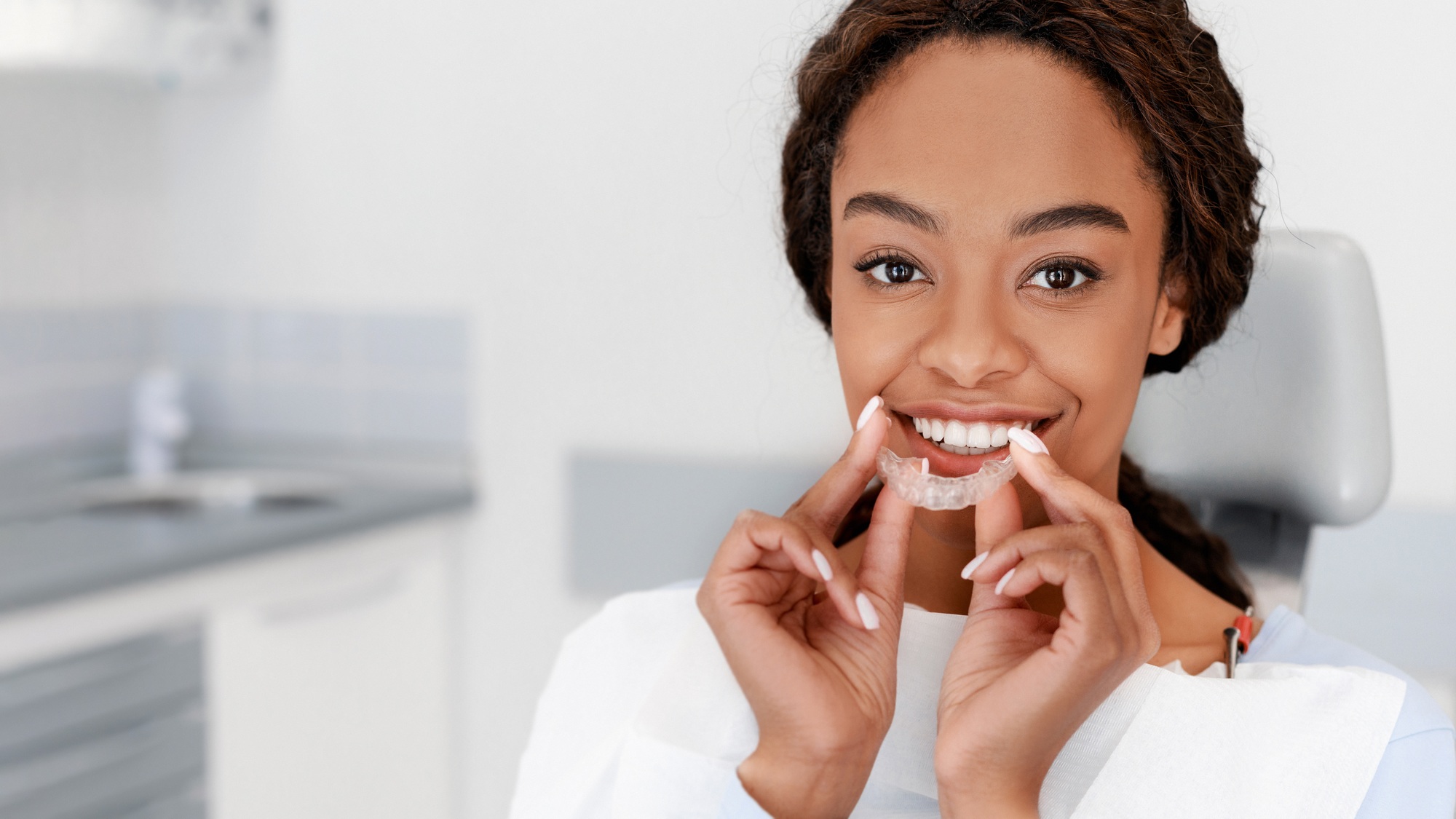 Smiling black girl holding invisible aligner, modern teeth trainer
