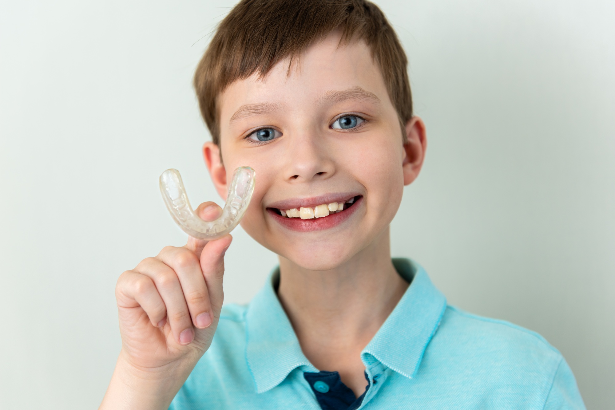 Smiling child boy over gray background holding an invisible aligner ready to use it. Dental health