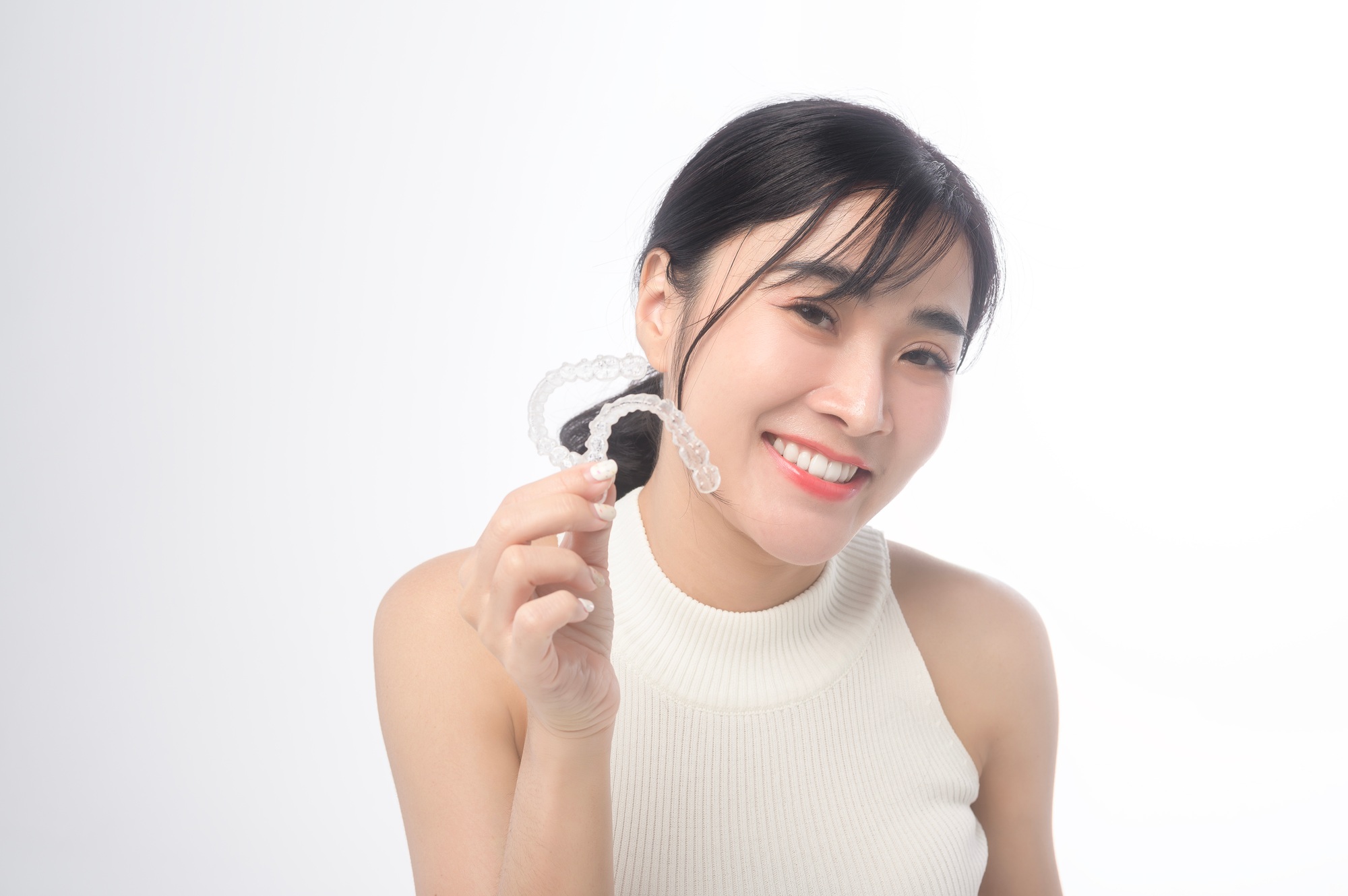 Smiling woman holding invisalign braces over white background
