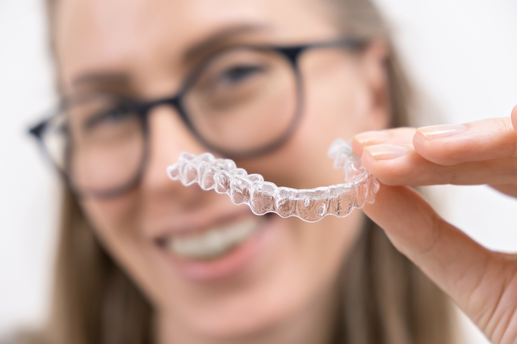 smiling woman using clear plastic removable braces aligner or whitening tray. dental orthodontic
