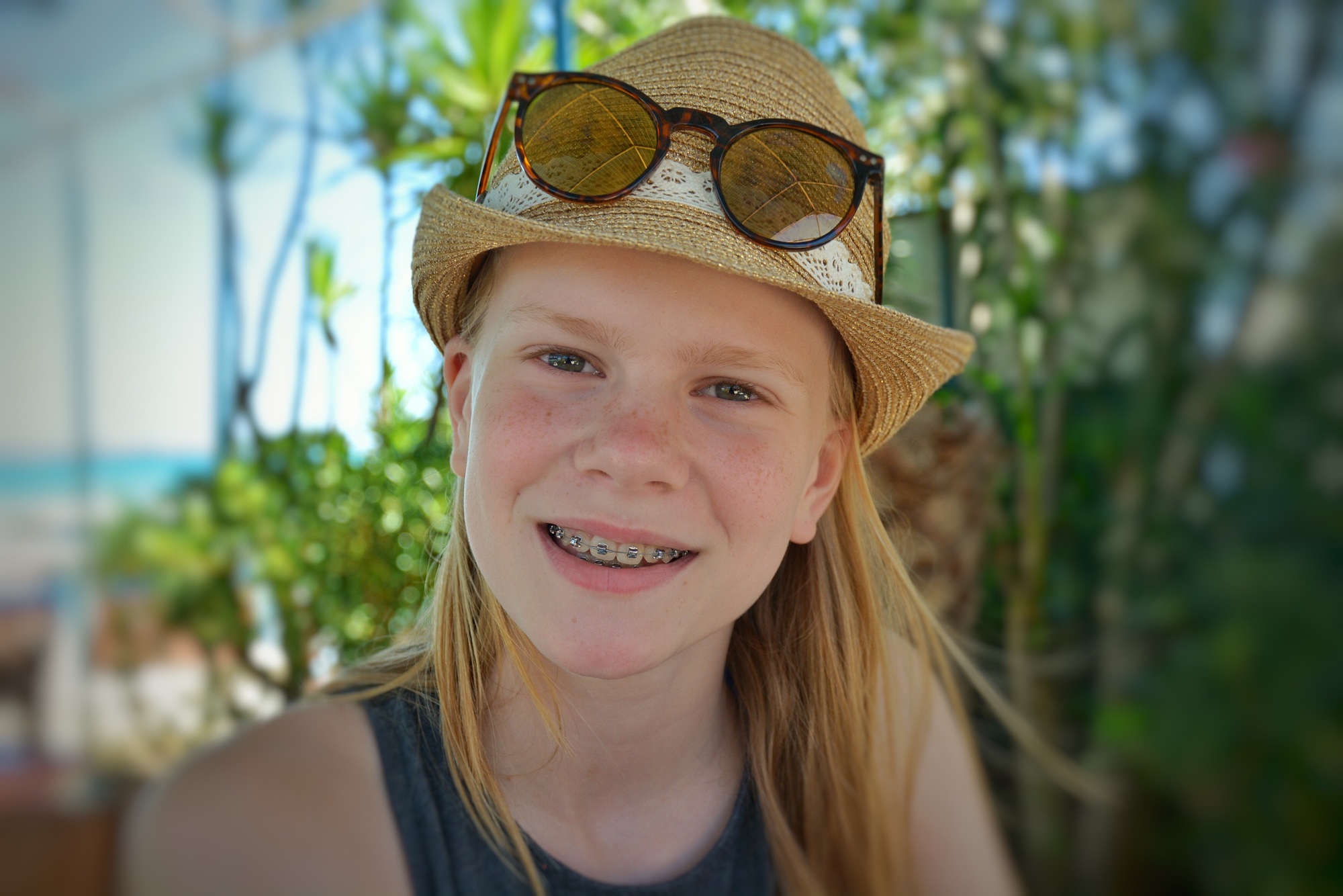 Smiling young girl with dental braces, wearing a summer hat with sunglasses