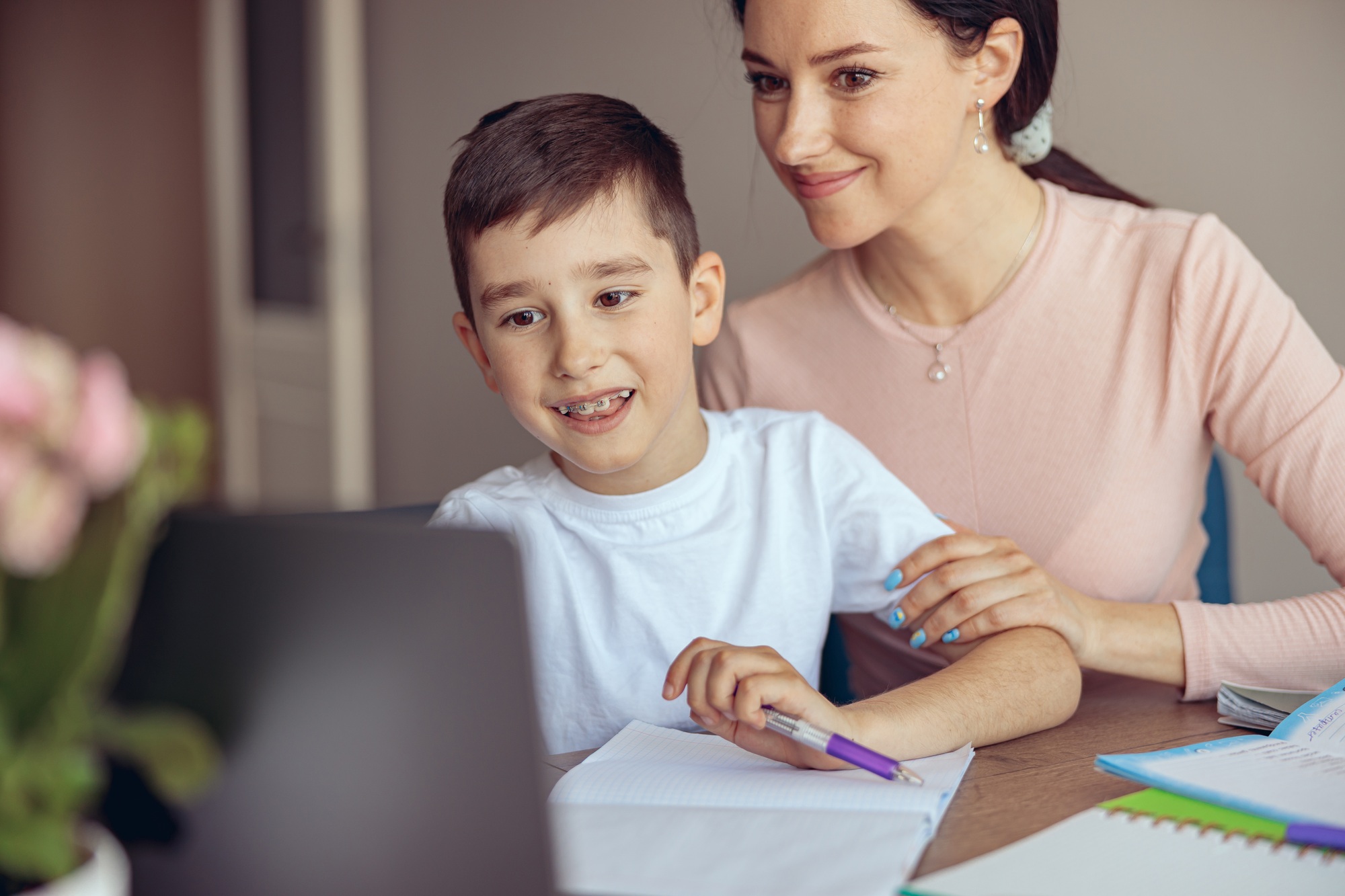 Teen cute boy with braces learning homework at laptop computer and mom helping.