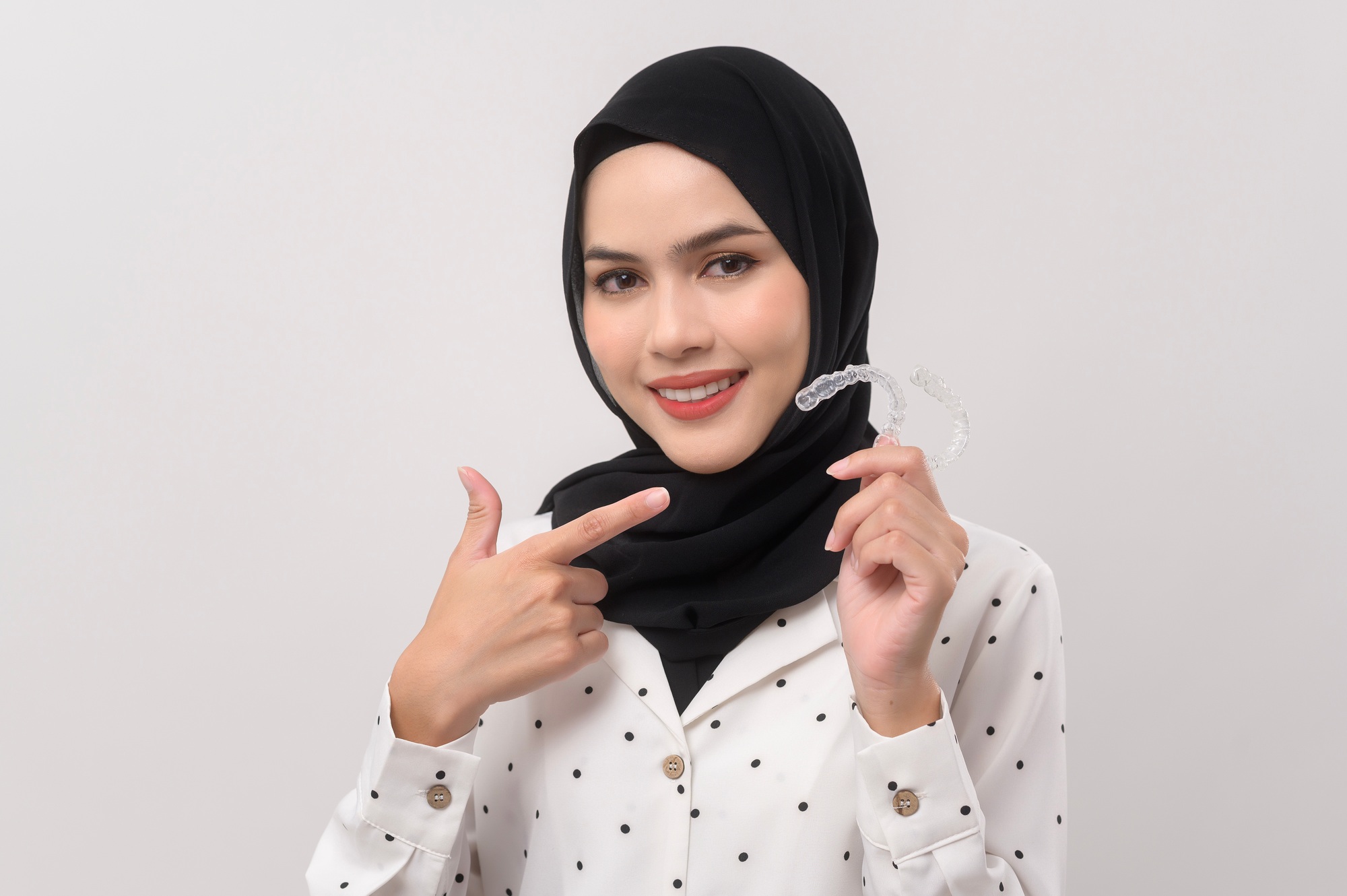 Young smiling muslim woman with hijab holding invisalign braces in studio